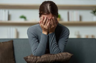 Genç bir kadın duygusal acısını yüzünü kapatarak ifade ediyor, zihinsel sağlık bilincinin önemini vurguluyor..