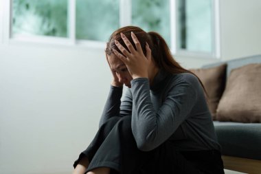 Genç bir kadın, bir koltukta otururken kafasını tutup zihinsel sağlık bilincine duyulan ihtiyacı vurgulayarak hayal kırıklığını ifade eder..