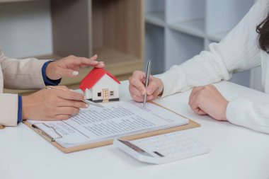 Müşteri ve danışman, ev satın alma anlaşmasını gözden geçirir. Model ev ve sözleşme belgelerini profesyonel ortamda inceler..