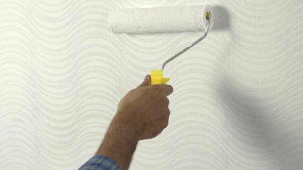 4k. Gros plan des mains de l'homme en utilisant un rouleau de peinture tout en peignant le papier peint de couleur blanche, travaillant à l'intérieur. — Video