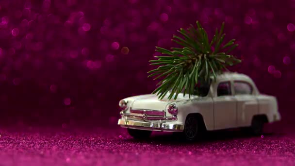 Coche de juguete blanco con árbol de Navidad en el techo cabalga sobre un fondo de brillo borroso. Concepto de entrega. — Vídeos de Stock