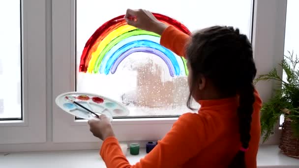 Κορίτσι ζωγραφική ουράνιο τόξο στο παράθυρο κατά τη διάρκεια καραντίνας στο σπίτι. — Αρχείο Βίντεο