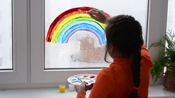 Fille peinture arc-en-ciel sur la fenêtre pendant la quarantaine à la maison. — Video