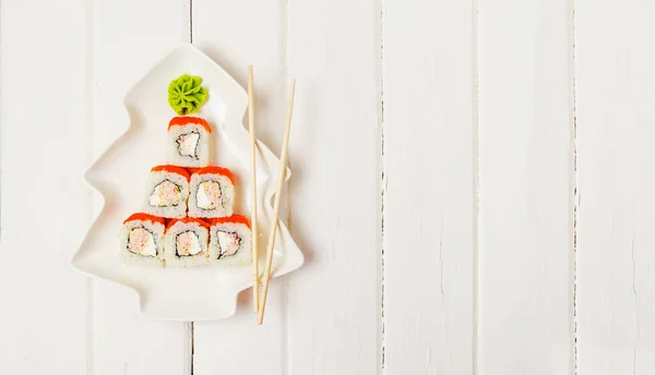 Funny edible Christmas tree made from sushi, creative idea for japanese restaurant on white background. New Year food background top view . holiday, celebration, food art concept. Copyspace.