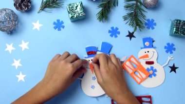 Bir çocuk bir kardan adamla Noel hediyesi yapıyor. Noel ağacı süslemeleri. Mavi ahşap arka planda kardan adam parçaları. Noel fikirleri yaratıyor..