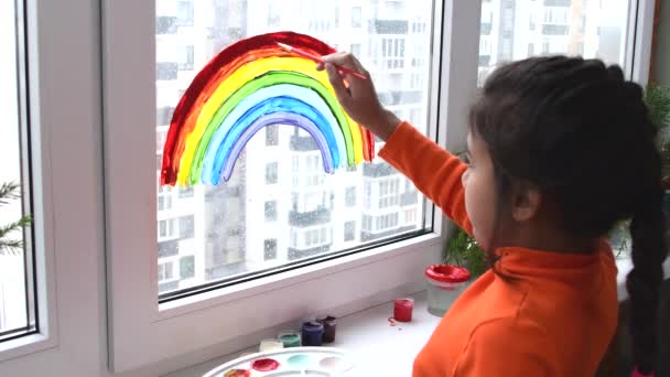Dziewczyna malowanie tęczy na oknie podczas kwarantanny w domu. — Wideo stockowe