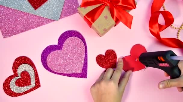 Valentines Day or birthday presents. Valentines Day gifts with a red paper heart on a wooden table. Girl makes red heart from red paper. Pink background. — Stock Video