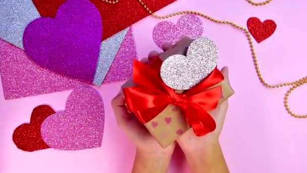 Walentynki albo prezenty urodzinowe. Walentynki prezenty z czerwonym papierowym sercem na drewnianym stole. Dziewczyna wprowadzenie prezent na różowym tle. — Wideo stockowe