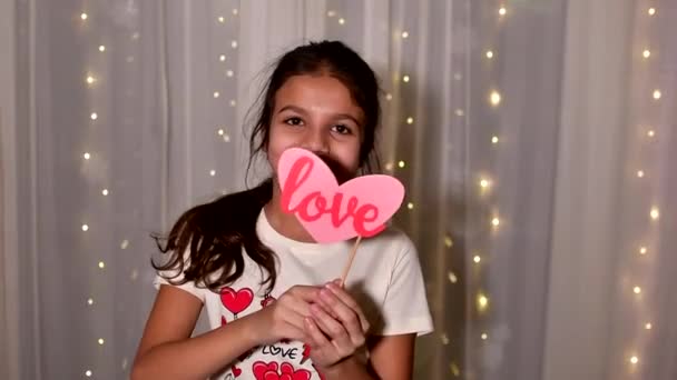 Cabina de fotos, forma de corazón cerca en las manos de llittle chica sonriente pelo oscuro en el Día de San Valentín. Movimiento lento. — Vídeo de stock