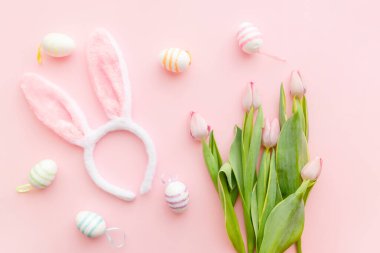 Paskalya gününde pembe arka planda tavşan kulakları ve pembe laleler. Baharda Paskalyayı kutluyoruz. Renkli yumurtalar.