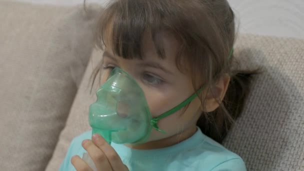 Egy kislány belélegzi a porlasztót otthon. Gyermek asztma inhalátor inhalációs porlasztó beteg köhögés koncepció. Beteg kislány lélegzik egy porlasztóban otthon.. — Stock videók