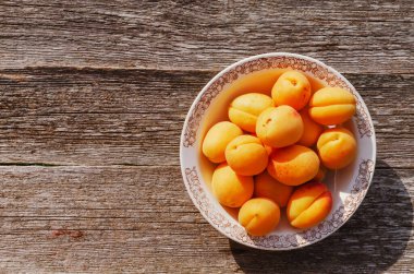 Masanın üzerinde, ahşap zeminde, rustik bir tabakta olgun kayısılar..