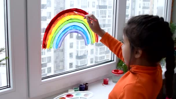 Dziewczyna malowanie tęczy na oknie podczas kwarantanny w domu. — Wideo stockowe