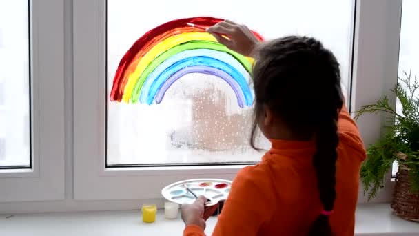 Κορίτσι ζωγραφική ουράνιο τόξο στο παράθυρο κατά τη διάρκεια καραντίνας στο σπίτι. — Αρχείο Βίντεο