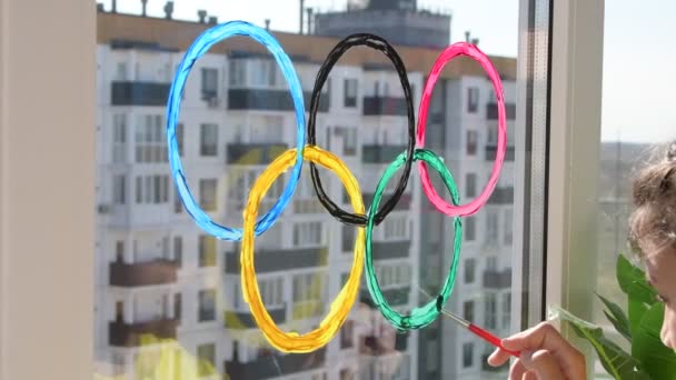 Дівчинка малює олімпійські кільця на вікні під час карантину. Росія. 2 може 2021 — стокове відео