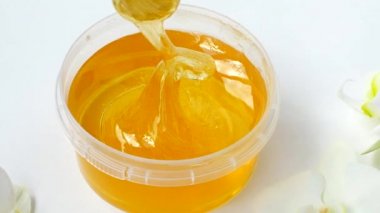 Beyaz arka planda şeffaf bir kavanozda şeker yapıştırıcısı. Bir usta istenmeyen kılları çıkarmadan önce şeker macununu karıştırır. Şekerleme. Depilasyon. Epilasyon. Güzellik konsepti.