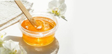 Şeffaf bir kavanozda bal ya da balmumu ezmesi ve beyaz arka planda beyaz orkide. Şekerleme. Deplasyon ve güzellik konsepti. Ağda.