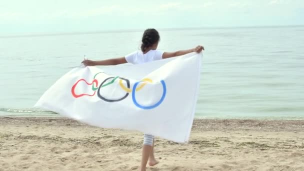 Mädchen schwenken Flagge der Olympischen Spiele im Freien über bewölkten Himmel und blauem Wasser des Meeres. Kindersportfan. 27.06.2020 St.Petersburg Russland — Stockvideo