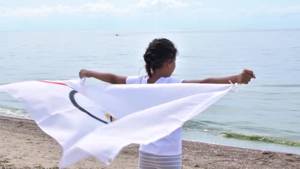 옥외에서 올림픽 대회 깃발을 흔들고 있는 소녀가 구름낀 하늘 과푸른 바 다 의물 위에 손을 흔들고 있다. 어린이 스포츠 팬. 27.06.2020 St.Petersburg 러시아 — 비디오