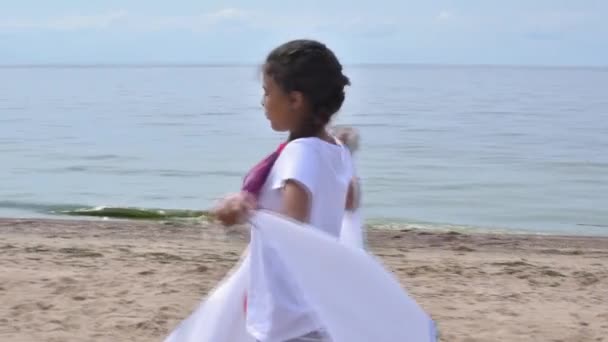 Chica ondeando bandera de los Juegos Olímpicos al aire libre sobre el cielo nublado y el agua azul del mar. Niños fanáticos de los deportes. 27.06.2020 San Petersburgo Rusia — Vídeo de stock