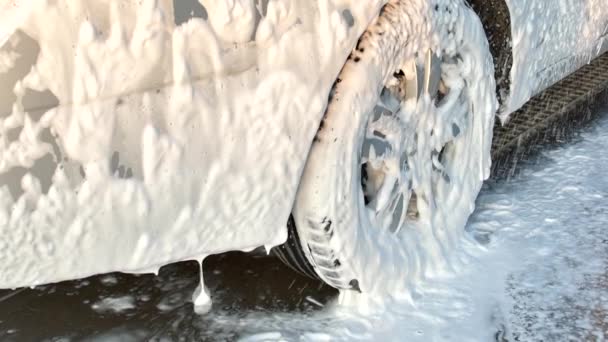 Processo de lavagem de carro de carro cheio coberto com espuma branca e salpicos de arma de água. Espalhamento de espuma no carro brilhante exterior câmera lenta. — Vídeo de Stock
