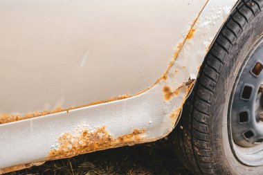 Gümüş arabanın gövdesinde ve kapılarında sert aşınma ve pas var. Araba rockçı panelinin aşınmasından paslı kapı pervazına yakın, araç gövdesinde pas deliği, aşındırıcı metal yıkım.