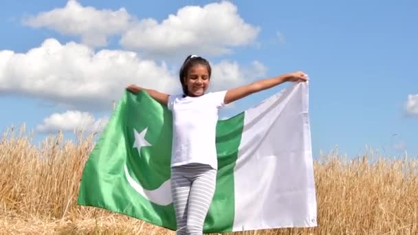 Flicka viftande flagga av Pakistan utomhus över blå molnig himmel och gyllene vete. Pakistans dag — Stockvideo