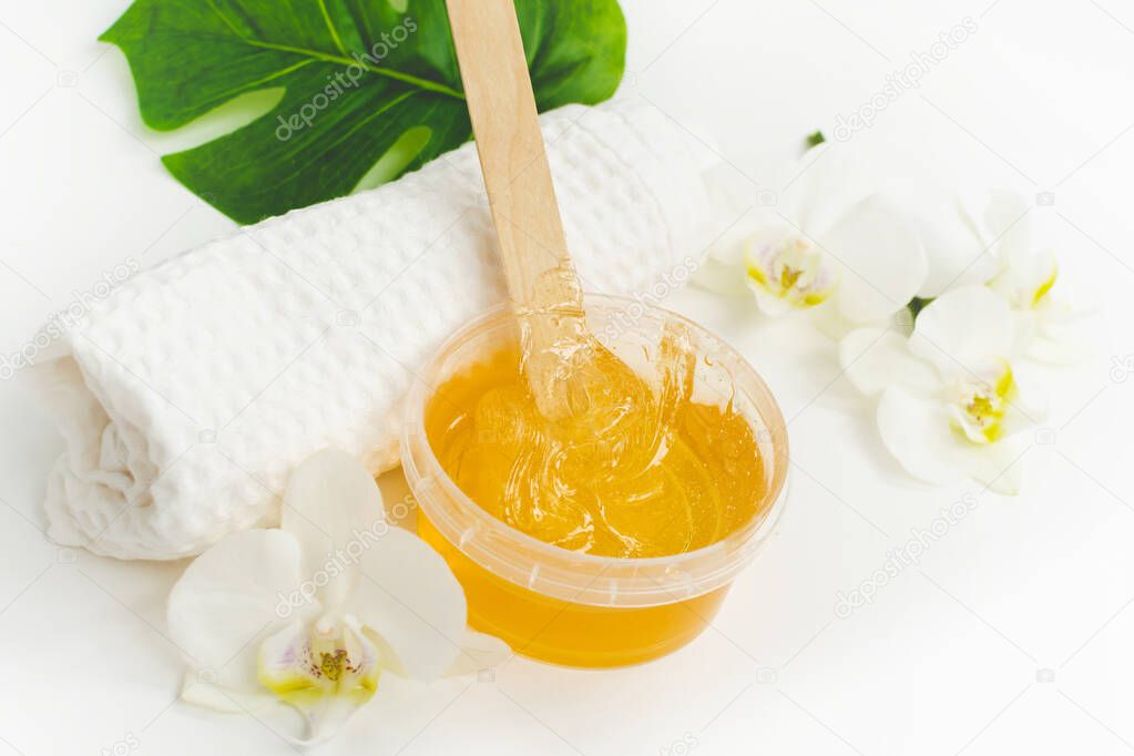 Sugar paste or wax honey in a transparent jar and white orchid on a white background. Sugaring. Depilation and beauty concept. Waxing. Close up shot.