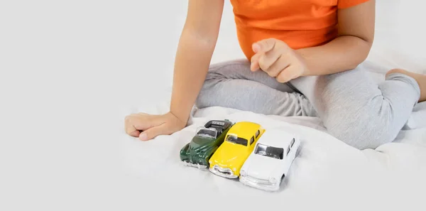 Little girl playing with white toy car. Sitting on the white bedsheet. Smiling. — Stock Photo, Image