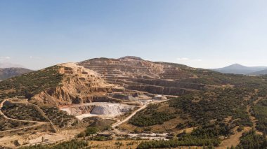 A large open-pit mine or quarry in a rural mountainous area with stepped layers. Raw material quarry for a cement factory. Mining, environment, industry.