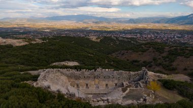 Kibyra Antik Şehir Odeon kalıntıları, Burdur, Glhisar. Yeşil tepeleri ve modern şehir manzarası olan antik Roma yapısı. Drone görünümü.