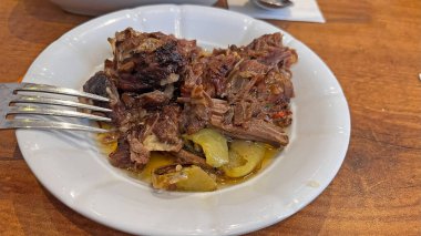 Bir tabak doğranmış et (kebap), zeytin yağı kaplı yeşil biberli beyaz bir tabakta servis edilir (veya sebze).).