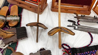 Geleneksel yün çevirme araçları (dönen tekerlekler), ahşap takunyalar ve bir pazar masasında eski araçlar.