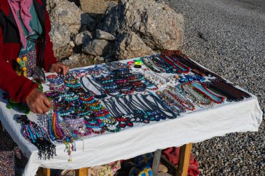 Yol kenarındaki tezgahta parlak renkli cam boncuklar, kolyeler ve bilezikler gibi zengin bir el yapımı mücevher koleksiyonu sergileniyor. Hediye satan bir tezgah..