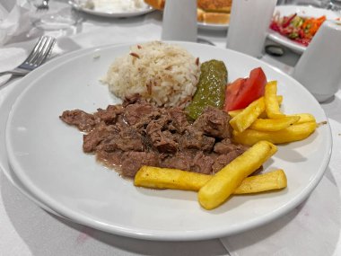 Geleneksel pilav, sotelenmiş et, kızarmış patates, salatalık turşusu ve taze domates dilimlerinin yer aldığı Türk mutfağından lezzetli bir ana yemek..