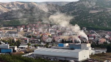 Endüstriyel tesisin ve hemen arkasındaki yerleşim alanının havadan görüntüsü. Şehir ve endüstriyel yaşamın iç içe geçtiği dağ manzarasının insansız hava aracı görüntüsü..