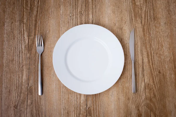 White plate with fork and knife on wooden background — Stock Photo, Image