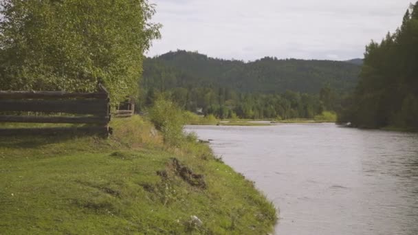 Дерев'яний паркан з одного боку великої річки, дерев і гори з іншого . — стокове відео