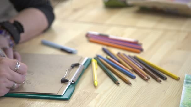 Diseñadora mujer pensar en el diseño de tarjetas con un saludo en la mesa con un montón de lápices de colores . — Vídeo de stock