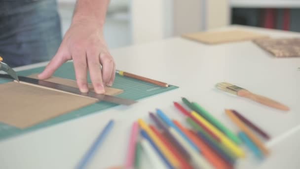 Mani da uomo tagliate con un righello e un coltello, carta marrone sul tavolo con matite colorate . — Video Stock