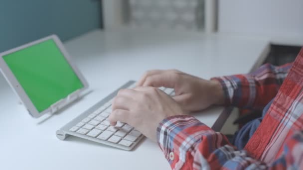 Mãos masculinas uma camisa xadrez digitando no teclado sem fio com tela verde do tablet . — Vídeo de Stock