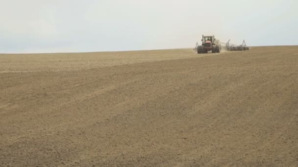 Un tracteur sème un champ labouré à l'aide d'un semoir .