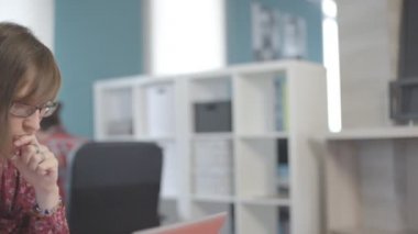 Gözlük ile duvar raf, ofisinde çalışan genç kadın elini dudaklarına koyarak.