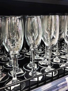 Neat rows of empty, clear wine glasses or crystal glasses displayed on black shelves