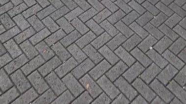 Yukarıdan aşağıya doğru çekilen videoda ringa balığı desenli tuğla kaldırımın ve yürüyen insanların gölgelerinin hareketli görüntüleri var. 4k 60 fps. 3840 x 2160.