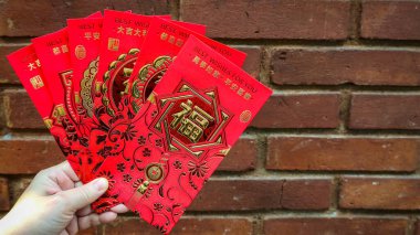 Fanning 'e geleneksel ay kırmızısı Hongbao zarflarını altın folyo el yazısı ve çiçek filigranıyla birlikte kırsal bir kırmızı tuğla zemin üzerinde ver. Çeviri: Servet