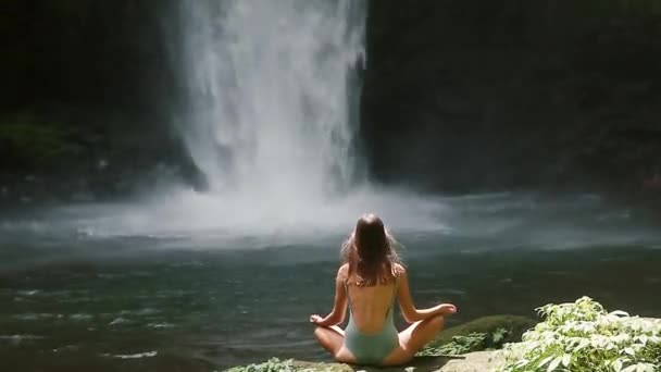 Girl meditating in front of waterfall — Stock Video