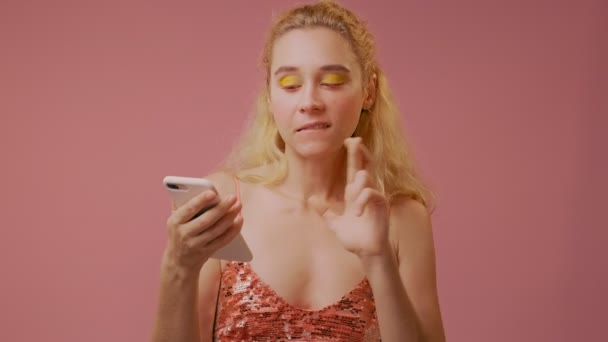 Молодая женщина использует современный мобильный телефон, делает обнадеживающий жест со скрещенными пальцами — стоковое видео