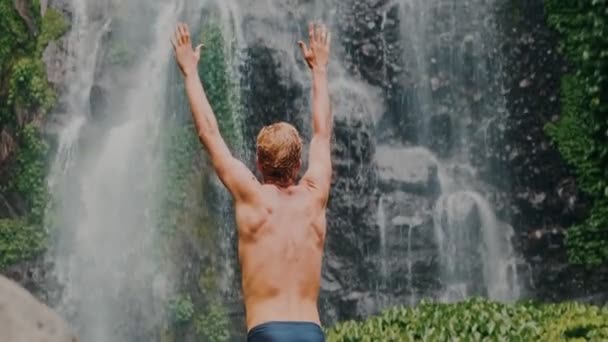 L'uomo a cascata alzando le mani nel sentirsi più vicino alla natura. Viaggio a Bali. — Video Stock