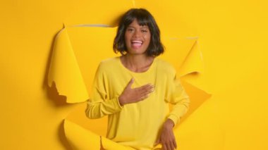 Genç kadın, altın sarısı arka planda yırtık bir delikte kıkırdıyor.